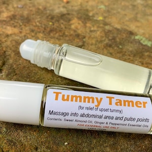 May include: Two white roller bottles with clear liquid inside. The label on one bottle reads "Tummy Tamer (for relief of upset tummy) Massage into abdominal area and pulse points Contents: Sweet Almond Oil, Ginger & Peppermint Essential Oils FOR EXTERNAL USE ONLY LINDA ODOM"