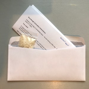 May include: A white envelope with a handwritten note that says "ENJOY! BEN" on the front. The envelope contains a small plastic bag with a white powder inside. The bag is labeled "Sourdough Activation Instructions".