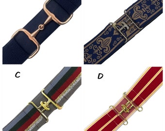Pode incluir: Quatro cintos elásticos rotulados A, B, C e D. O cinto A é azul-marinho com uma fivela de bridão em ouro rosa. O cinto B é azul-marinho com padrão de flor-de-lis dourada e fivela de bronze. O cinto C é cinza com listras e fivela dourada. O cinto D é vermelho com listras douradas e fivela dourada.