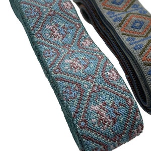 May include: Two rolls of woven jacquard ribbon trim. The left roll features a repeating diamond pattern in shades of teal, light blue, and dusty rose. The right roll displays a geometric motif in grey, orange, and blue. Both ribbons are textured.