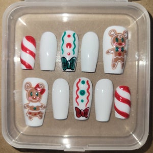 May include: A set of ten white false nails with festive Christmas designs. The designs include gingerbread people, candy canes, and green and red swirls.