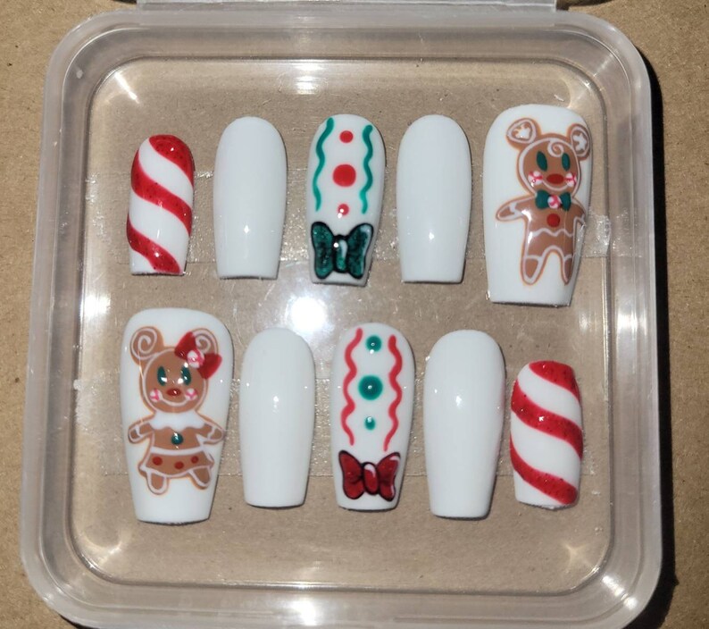 May include: A set of ten false nails with a Christmas theme. The nails are white with various designs including candy canes, gingerbread people, and green and red swirls.