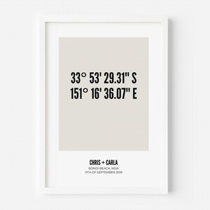 May include: A framed vertical wall art print featuring black text on a light beige background. The text displays coordinates 33° 53' 29.31" S 151° 16' 36.07" E, followed by the names CHRIS + CARLA, the location BONDI BEACH, NSW, and the date 11TH OF SEPTEMBER 2019.