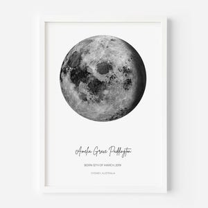May include: A framed wall art print featuring a detailed black and white image of the moon. Below the moon, the text reads Amelia Grace Paddington, BORN 12TH OF MARCH, 2019, and SYDNEY, AUSTRALIA, printed in a clean, modern font style.