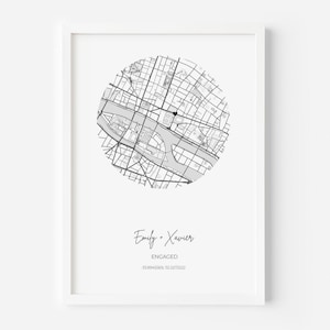 May include: A framed wall art print featuring a circular black and white street map with a small heart icon. Below the map, the text reads Emily + Xavier, ENGAGED, and the coordinates -33.8945569, 151.2272222 in a clean, modern font style.