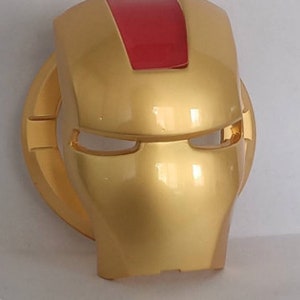May include: A gold plastic mask with a red top and eye holes. The mask is shaped like a superhero's face.