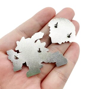May include: Two silver metal enamel pins with a pixelated design. The pins have a safety clasp on the back.
