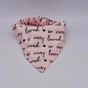 May include: Pink bandana with black text that says "so very loved" repeated. The bandana has a ruffled edge.