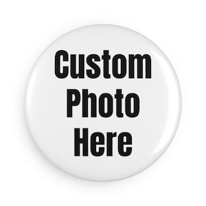May include: A white, round button with the text "Custom Photo Here" in bold, black letters. The button has a glossy finish and is likely a promotional item or a customizable accessory.