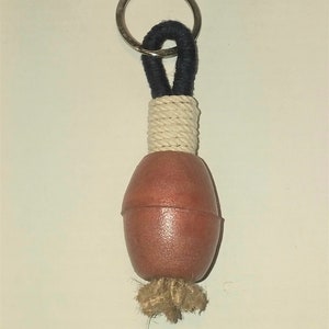 Può includere: Un portachiavi in corda marrone e bianca con una boa rotonda in legno rosso. Il portachiavi ha un anello in metallo argentato.