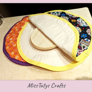 May include: Three round, fabric pot holders with yellow trim. The top pot holder is folded over to reveal a white fabric lining. The bottom pot holder has a floral pattern in orange and white. The middle pot holder has a black and white pattern with colorful skulls and flowers. The text "Miss Tatys Crafts" is visible at the bottom of the image.