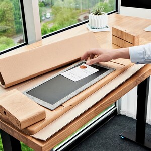 May include: A person assembling a wooden desk with a black chalkboard insert. The desk is made of light wood and has a black metal frame. The person is holding the chalkboard insert in their hand.