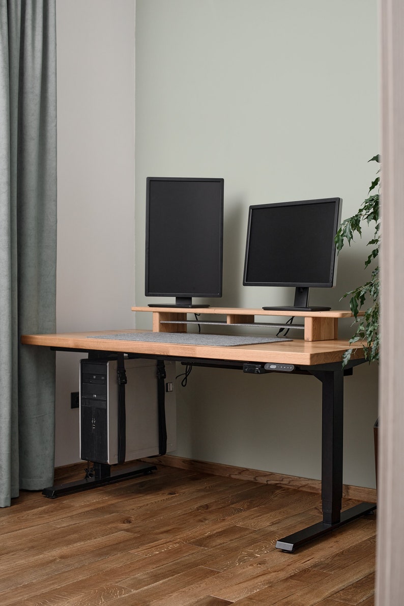 May include: A black standing desk with a wooden top and a black computer tower underneath. Two black computer monitors are on a wooden shelf above the desk.
