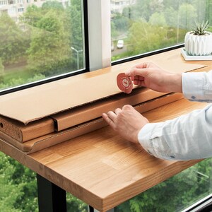 May include: A person assembling a wooden table from a flat-pack box. The table is made of light wood and has a natural finish. The person is using their hands to put the table together. The table is on a wooden surface.