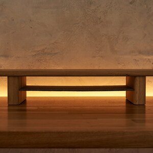 May include: A wooden shelf unit with two shelves. The shelf is made of natural wood and has a simple, modern design.