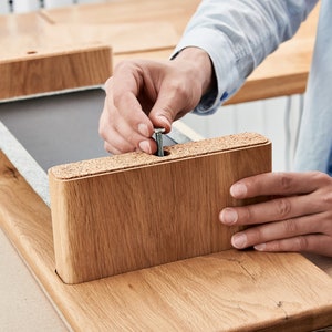 May include: A person is assembling a wooden desk by screwing a metal screw into a pre-drilled hole in a wooden desk leg.