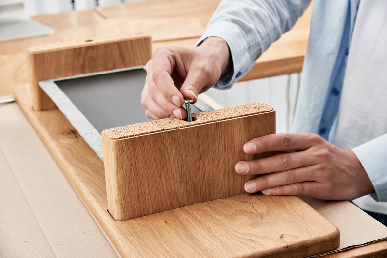 May include: A person is assembling a wooden desk by screwing a metal screw into a pre-drilled hole in a wooden desk leg.