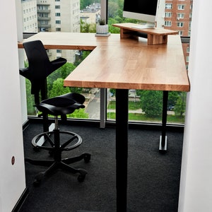 May include: A black office chair with a unique design sits next to a wooden desk with a black metal frame. The desk has a monitor stand and a potted plant on the surface. The desk is in front of a large window with a view of a city skyline.