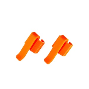 May include: Two orange plastic clips for organizing cables or wires. The clips are designed to be attached to a surface and have a curved shape to hold the cables in place.