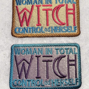 May include: Two embroidered patches with the text "Woman in total control of herself" and the word "Witch" in a stylized font. The top patch is beige with red lettering and a brown border. The bottom patch is gray with purple lettering and a teal border.