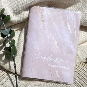 Könnte beinhalten: Ein rosa-weißes Marmor-Muster-Journal mit dem Text "Impress" und "Franziska Idahosa" in weißer Kursivschrift.