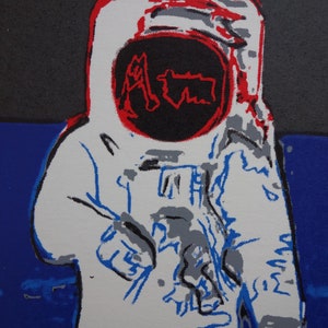 May include: A white astronaut figure with a red and black helmet. The helmet has the word "Aim" written in red inside a black circle. The astronaut is standing on a blue background.