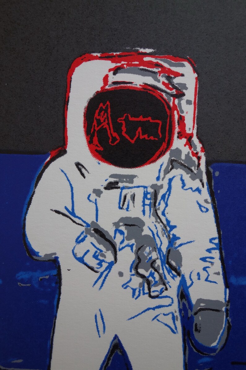 May include: A white astronaut figure with a red and black helmet. The helmet has the word "Aim" written in red inside a black circle. The astronaut is standing on a blue background.