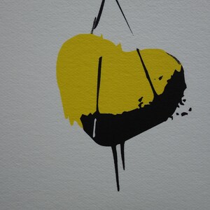 May include: Abstract art print with a yellow and black heart shape. The heart is hanging from a string.