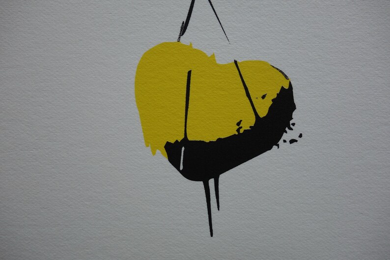 May include: Abstract art print with a yellow and black heart shape. The heart is hanging from a string.