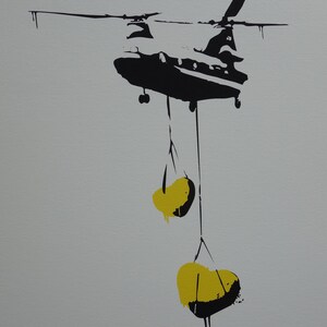 May include: A black silhouette of a helicopter carrying two yellow sacks hanging from ropes. The helicopter is against a light gray background.