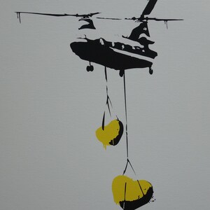 May include: A black silhouette of a helicopter carrying two yellow, heart-shaped objects.