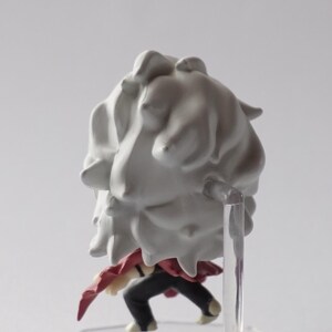 May include: A small figurine of a character with a large, white, cloud-like hairpiece. The figure is wearing a red garment and black pants. It is mounted on a clear plastic stand.
