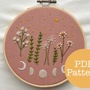 Può includere: Un cerchio da ricamo rosa con un disegno floreale che presenta margherite bianche, respiro di bambino bianco, foglie verdi e lune bianche. Il disegno include anche stelle gialle e una singola stella gialla più grande. Il cerchio ha una cornice in legno e il testo "PDF Pattern" è visibile nell'angolo in basso a destra.