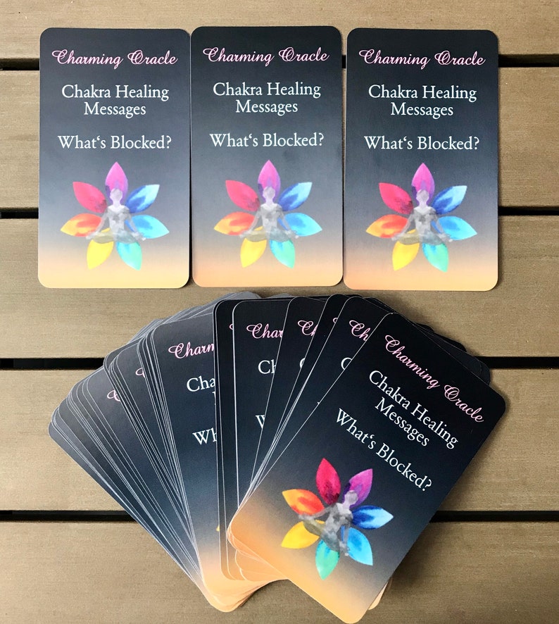 K&ouml;nnte beinhalten: Ein Kartendeck mit rechteckigen Orakelkarten, die den Text Charming Oracle, Chakra Healing Messages und What's Blocked? zeigen. Jede Karte zeigt eine zentrale Figur in sitzender Meditationshaltung, umgeben von einem bunten Bl&uuml;tenmotiv.
