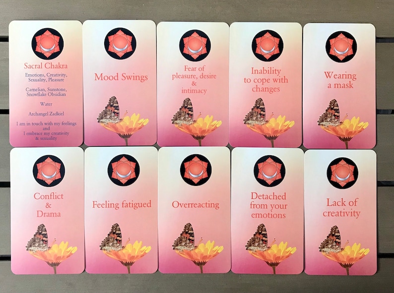 K&ouml;nnte beinhalten: Ein Set aus zehn rechteckigen Karten mit einem rosafarbenen Farbverlauf, die jeweils einen Schmetterling auf einer gelben Blume, ein kreisf&ouml;rmiges Chakrasymbol und Text zeigen. Die erste Karte ist als Sacral Chakra beschriftet, die anderen listen Zust&auml;nde.