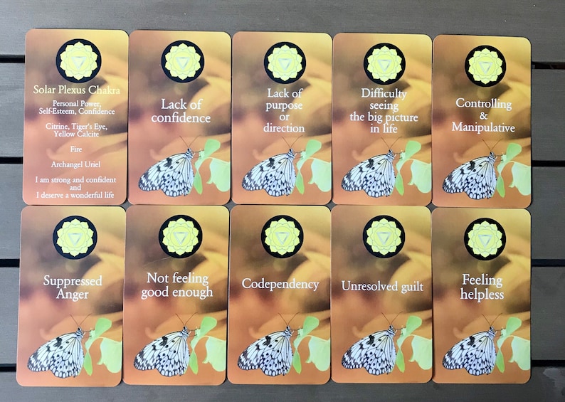 K&ouml;nnte beinhalten: Zehn rechteckige Karten mit einem gelben Solarplexus-Chakra-Symbol, einem wei&szlig;-schwarzen Schmetterling auf einem gr&uuml;nen Blatt und Text. Die erste Karte zeigt Solar Plexus Chakra, Personal Power, Self-Esteem, Confidence, Citrine, Tiger's Eye, Yellow Calcite, Fire, Archangel Uriel, I am strong and confident and I deserve a wonderful life. Weitere Karten enthalten Begriffe wie Lack of confidence, Lack of purpose or direction, Difficulty seeing the big picture in life, Controlling & Manipulative, Suppressed Anger, Not feeling good enough, Codependency, Unresolved guilt und Feeling helpless.