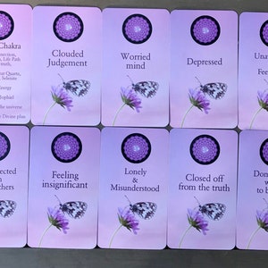 K&ouml;nnte beinhalten: Zehn rechteckige Karten mit einem hellvioletten Farbverlauf. Jede Karte zeigt oben ein violettes Mandala, einen Schmetterling auf einer violetten Blume und Text. Die erste Karte tr&auml;gt die Aufschrift Crown Chakra, Divine connection, Inner wisdom, Life Path, Spiritual truth, Amethyst, Clear Quartz, Moonstone, Selenite, Cosmic Energy, Archangel Jophiel, I am one with the universe and I have trust in the Divine plan.