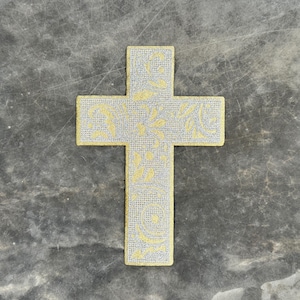 Könnte beinhalten: Ein goldenes Kreuz mit einem floralen Design auf grauem Hintergrund.