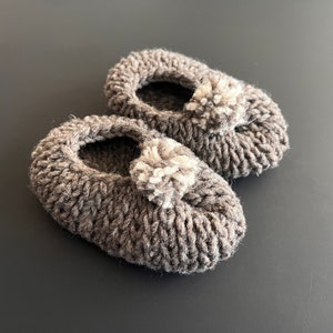 May include: A pair of gray knitted baby booties with white pom-poms.