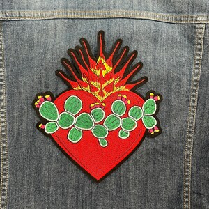 May include: Embroidered patch featuring a red heart with a prickly pear cactus design. The heart is surrounded by a yellow and red flame-like design.
