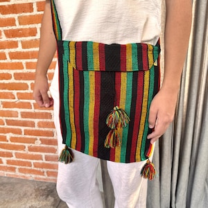 May include: A colorful, striped shoulder bag with a flap pocket and decorative tassels. The bag features vertical stripes in red, green, yellow, and black. The strap is also striped. The bag is worn over the shoulder.