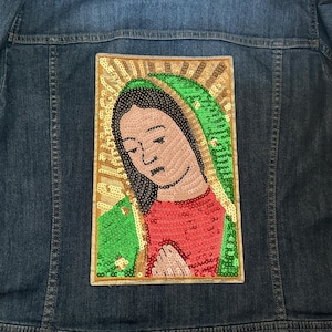 May include: A denim jacket with a sequined patch of the Virgin Mary. The patch is gold, green, and red.