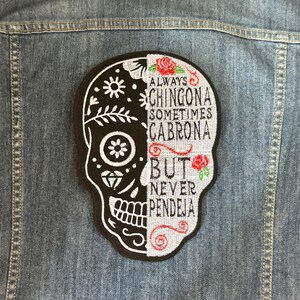 May include: Black and white sugar skull patch with red roses and the text "Always Chingona Sometimes Cabrona But Never Pendeja".