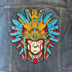 May include: A colorful embroidered patch featuring a stylized Native American warrior wearing a headdress with blue, red, yellow, and white feathers. The warrior's face is painted with red and white stripes.
