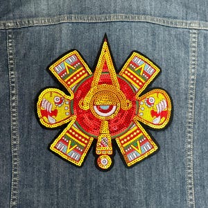 May include: A red, yellow, and gold sequined patch with a geometric design. The patch features a stylized face with a large eye and a pointed nose.