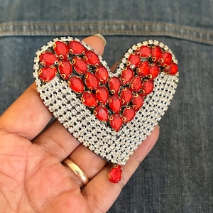 Può includere: Un broche a forma di cuore rosso e argento con strass e gemme rosse.