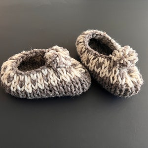 May include: A pair of gray and white knitted baby booties with a pom-pom on each.