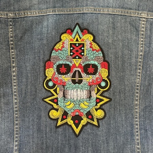 May include: A colourful embroidered patch featuring a detailed skull design with intricate patterns and a turquoise, yellow and red colour scheme.