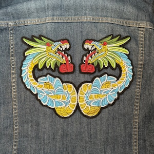 Puede incluir: Un par de parches bordados para planchar que representan dos dragones verdes, amarillos y azules enfrentados con lenguas rojas.
