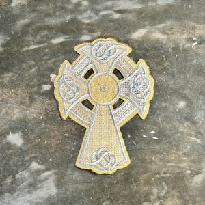 Puede incluir: Una cruz celta dorada con detalles plateados. La cruz es un símbolo tradicional irlandés de fe y herencia.